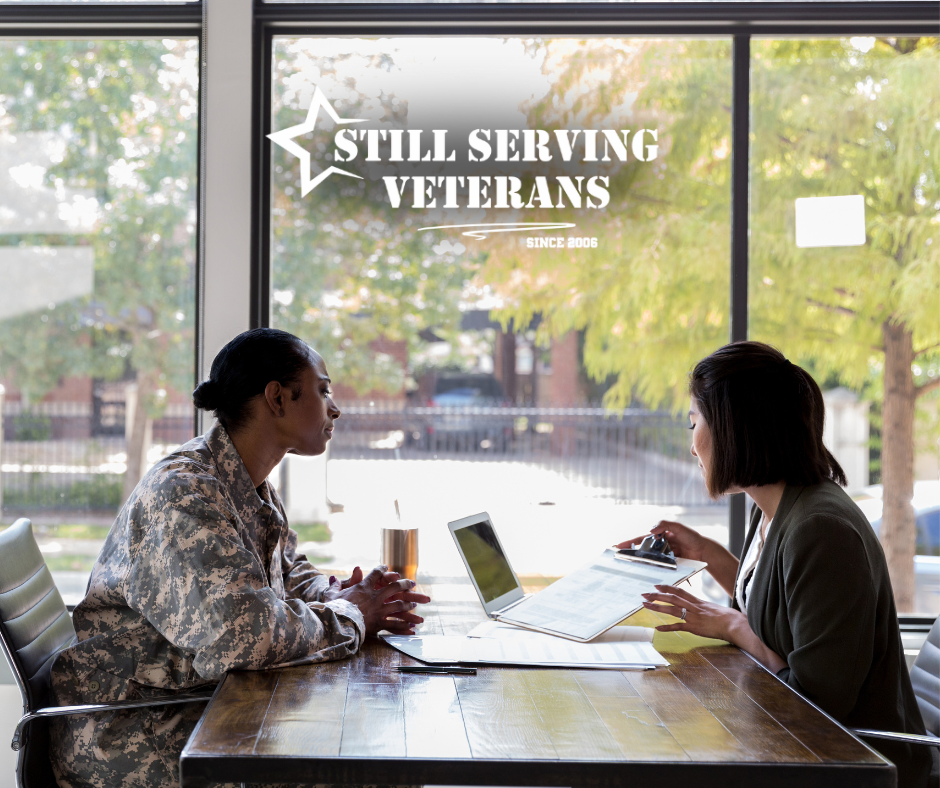 Veteran in military uniform meeting with a career counselor at Still Serving Veterans office, reviewing documents at a table near a window.