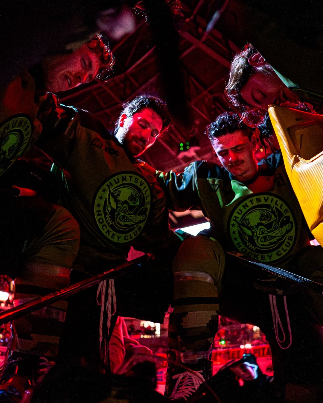 Huntsville Havoc hockey players gathered in a pre-game huddle under arena lights.