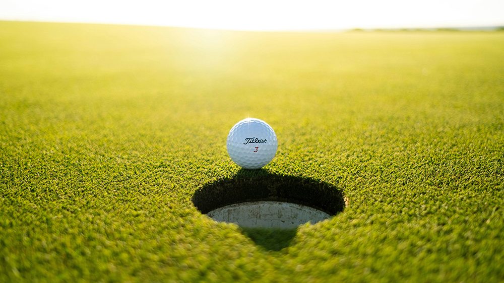 Golf ball on the edge of a hole on a green golf course.